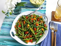 a white plate topped with green beans next to a glass of orange juice and silverware