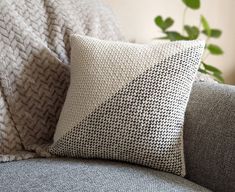 a gray couch with a black and white pillow on it's back next to a potted plant