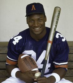 a man sitting on a bench with a baseball bat and glove in his hand, smiling at the camera