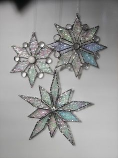 three snowflakes are hanging from strings on the wall, one is decorated with iridescents