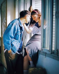 a man and woman standing next to each other in front of a window with shutters