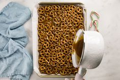 someone pouring caramel sauce on pretzels in a baking pan