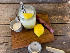 a wooden cutting board topped with two lemons next to a mason jar filled with liquid