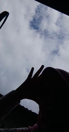 a person holding their hand up to the sky with clouds in the backround