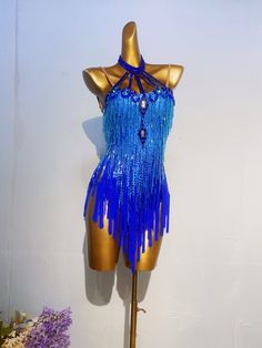 a mannequin with blue fringes and beads on it's torso, next to purple flowers