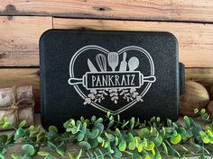 a black lunch box sitting on top of a wooden table next to some green leaves