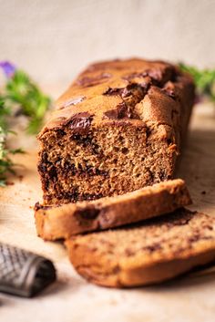 a loaf of chocolate chip banana bread on a cutting board next to a knife and flowers