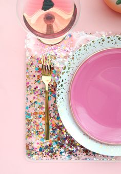 a pink table setting with confetti and gold rimmed plates, utensils