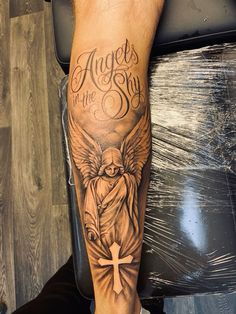 a man's leg with an angel and cross tattoo on it, which reads angels in the sky