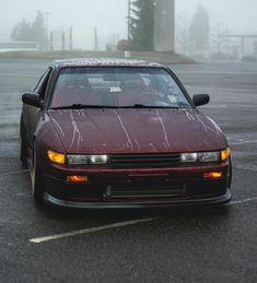 a red car parked in a parking lot on a foggy day