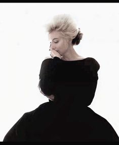 a woman with her eyes closed standing in front of a white background wearing a black dress