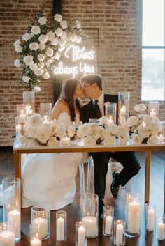 a bride and groom kissing in front of a table with white flowers and lit candles