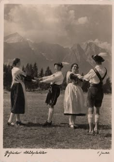 an old photo of four women in historical dress holding hands with mountains in the background