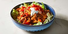 a blue bowl filled with meat and lettuce covered in sour cream on top of a white table