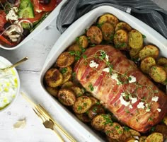 a roasting pan filled with meat and potatoes next to other food on a table