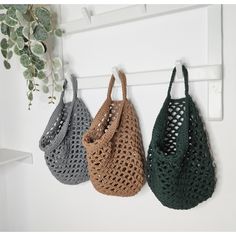 three crocheted purses hanging from hooks on a white wall next to a potted plant