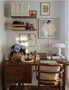 a wooden desk topped with two chairs next to a wall filled with pictures and vases