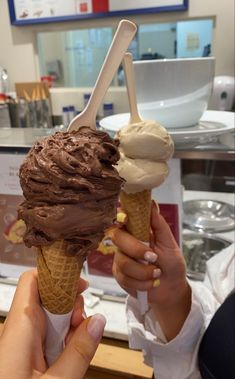 two people holding up ice cream cones in front of a counter with other items on it