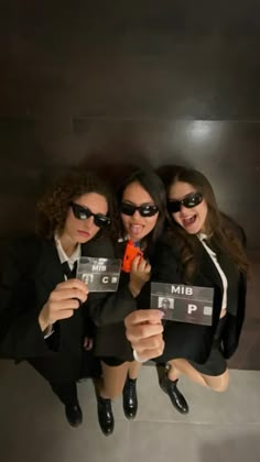 three women in black suits and sunglasses holding up signs