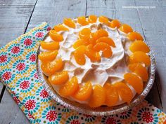 an orange pie with whipped cream on top is sitting on a colorful napkin and has flowers around it