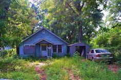 a car parked in front of a blue house surrounded by trees and grass with a small shed on the other side