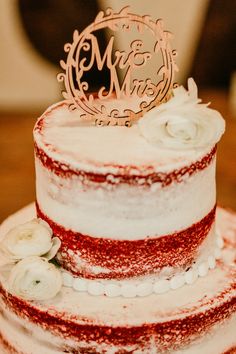 a red and white wedding cake with flowers on it's tiers is topped with a mr and mrs topper