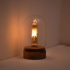 a light bulb in a glass dome on a wooden base with a white wall behind it