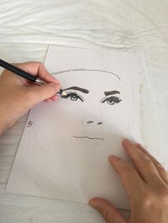 a person drawing a face on paper with a pencil