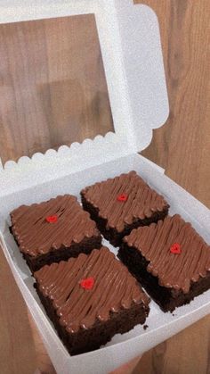 a person holding a white box with four brownies in it on a wooden table