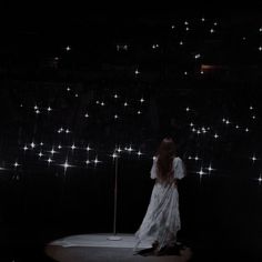 a woman standing on top of a stage next to a pole with lights all over it