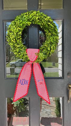 a red and white checkered ribbon on a door with a green wreath hanging from it's side