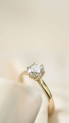 a close up view of a diamond ring on top of a white cloth with a gold band