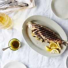 a fish is on a plate with lemon slices and sauces next to silverware