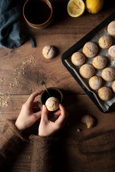 a person holding a bowl filled with powdered sugar next to lemons and muffins