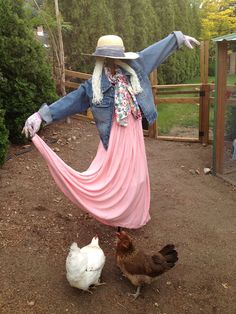 a scarecrow dressed as a woman with her arms spread out, standing next to two chickens