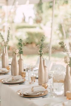 the table is set with white plates and vases