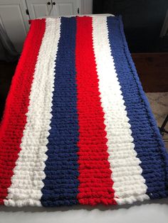 a red, white and blue crocheted blanket sitting on top of a bed