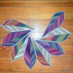 a knitted leaf is sitting on the floor next to a wooden floor with wood floors