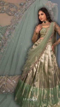 a woman in a green and gold lehenga standing next to a veiled wall