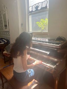 a woman sitting at a piano in front of a window with sunlight streaming through it