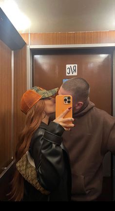 a man and woman kissing in front of an elevator door while taking a selfie with their cell phone