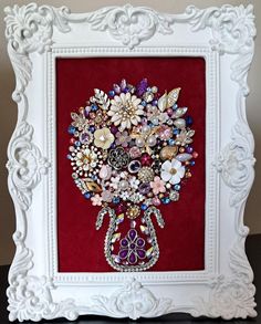 a white frame holding a bouquet of flowers on a red background with pearls and jewels