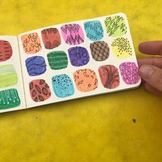 a hand holding an open notebook with different colored designs on the pages and in front of a yellow background