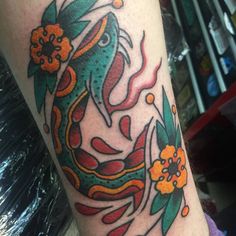 a colorful dragon tattoo on the arm with flowers and leaves around it's neck