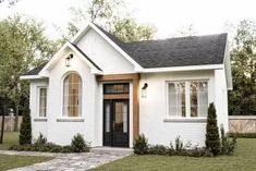 a small white house with a black door and windows in the front yard is shown