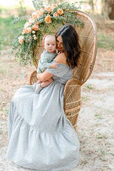 a woman sitting in a wicker chair with a baby on her lap and flowers around her neck