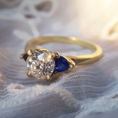 a diamond and blue sapphire ring sitting on top of a lace covered tablecloth with white fabric