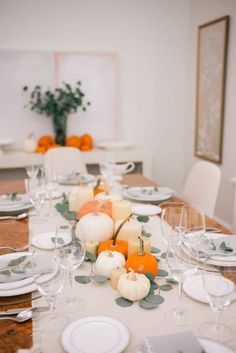 the table is set with white and orange pumpkins, candlesticks and plates