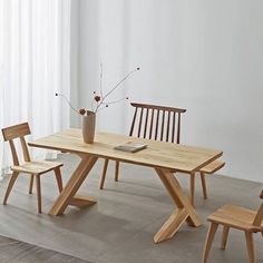 a wooden table with four chairs and a vase on the top, in front of a window