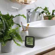 an alarm clock sitting on top of a bathroom counter next to a sink and potted plant